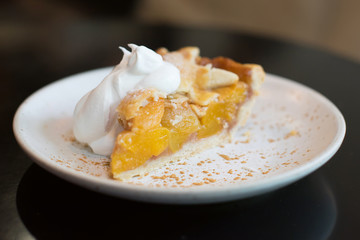 peach pie with whipping cream on white plate.