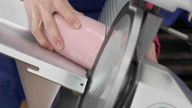 Professional electric food slicer. Meat slicing machine cutting processed meat products. Closeup of female chef slices boiled sausage.