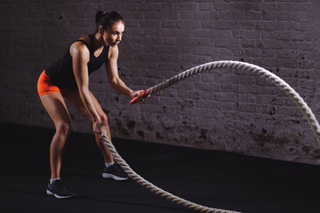 Woman training with battle rope in cross fit gym