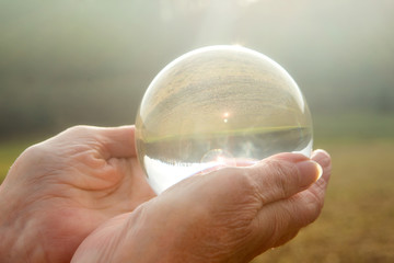 older womans hand holding a shiny glass sphere