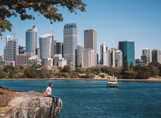 Young man sitting in the park on the edge of the cliff with an amazing Sydney city view