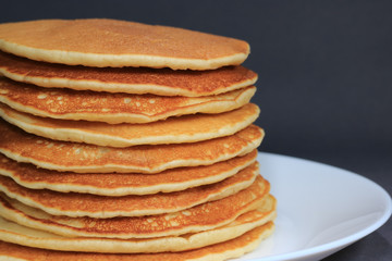 Front view of Stack of homemade plain pancakes served on white plate on black background with selective focus 