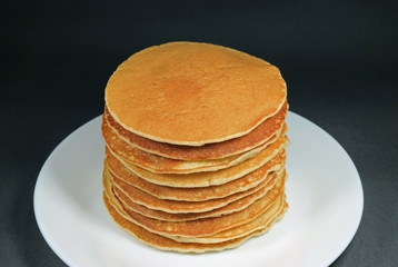 Stack of homemade plain pancakes served on white plate on black background 