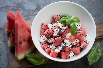 Watermelon salad with feta cheese and sesame seeds served in a white bowl, studio shot