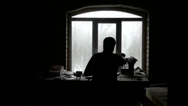 A writer writes in the dark by the window