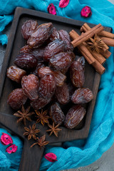 Above view of dates with aniseeds and cinnamon sticks on a black wooden serving tray, vertical shot