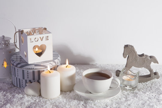 wooden white candlestick, candles, cup of tea and wooden horse on white artificial snow