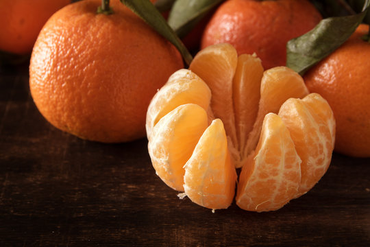 peeled clementine and whole fruits on a dark brown wooden board,  close up