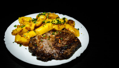 grilled meat fillet steak with fried potato in a plate on dark wooden background with copy space.