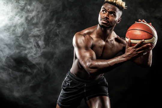 Portrait of afro-american sportsman, basketball player with a ball over black background. Fit young man in sportswear holding ball.