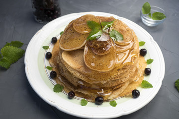 Pancakes are located in a plate on a gray background, decorated with berries and mint leaves. Pancakes in maple syrup.