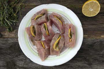The fillet of turkey stuffed with thyme, rosemary and lemon on a light plate which are located on a wooden background close up.