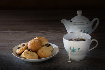 Cookies and English tea set on wooden background in dim light