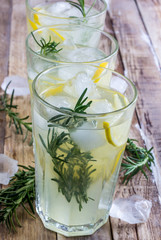 Cold lemon drink with rosemary, ice and tonic, on rustic wooden table. Selective focus