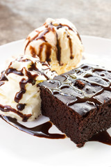 Brownie served with ice cream and whipped cream on white plate. Topping with chocolate sauce.