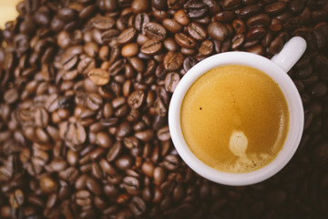 Espresso coffee with cream on a white cup on a brown coffee beans background