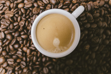Espresso coffee with cream on a white cup on a brown coffee beans background