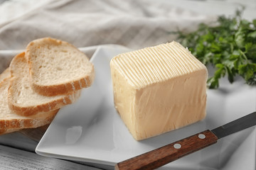 Plate with piece of fresh butter and sliced bread on table, closeup