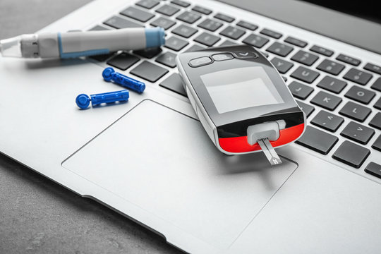 Digital glucometer and lancet pen on laptop. Diabetes management