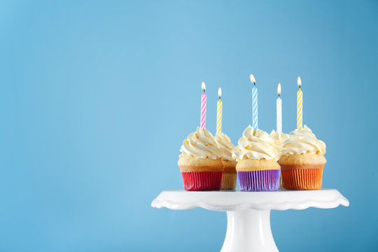 Birthday cupcakes with candles on stand against color background