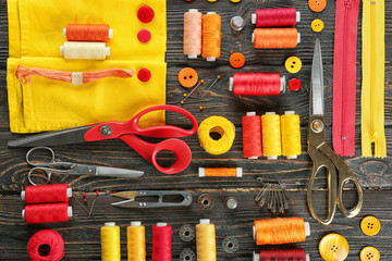 Composition with sewing threads, fabric and accessories on wooden background, top view