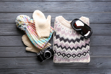 Warm clothes with ski goggles and photo camera on wooden background. Winter vacation concept