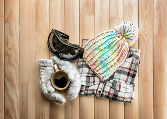 Warm clothes with ski goggles and cup of coffee on wooden background. Winter vacation concept