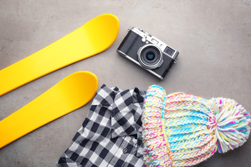 Warm clothes with photo camera and skis on grey background. Winter vacation concept