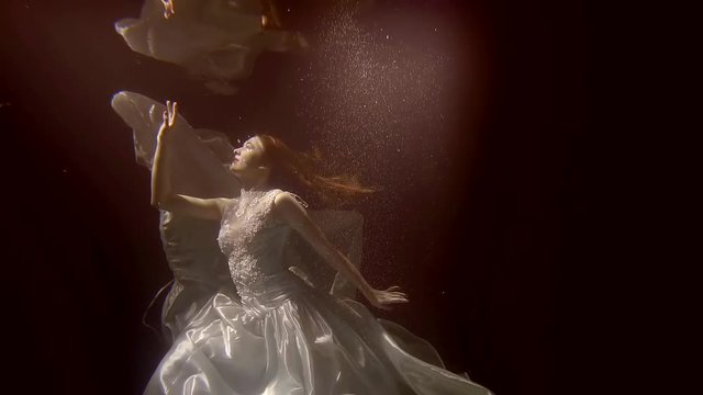 A young bride in a dress is floating under the water and is going to touch her reflection