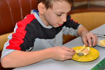 Cute little boy child with long blond hair eats fruit cake pie with chocolate at wooden table