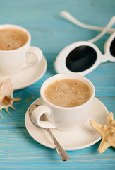 Sunglasses and two white cups of coffee on a wooden blue background.