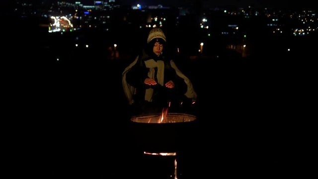 Hobo withe woman warm near fire at long cold night with far away city lights background lowlight 