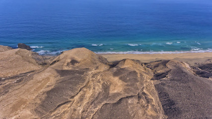 View from volcanic rocky mountain towards sandy beach and blue sea .