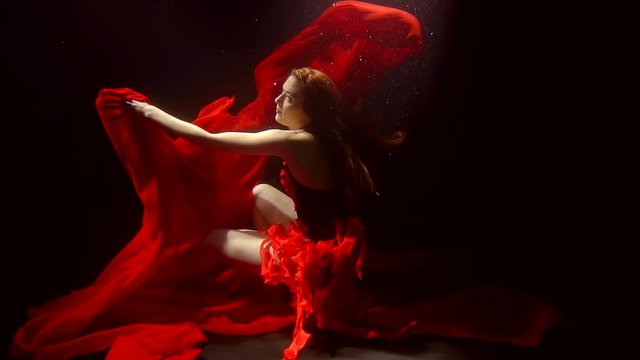 A young woman with red hair dances deep in the sea waters, the fabric flutters