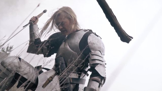 A woman knight in armor is kneeling in the field and experiencing grief, slow motion
