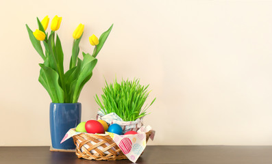 A wicker basket with colorful Easter eggs, yellow tulips in vase, Easter decoration on light background. Free space for your text.
