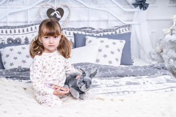 Portrait of a beautiful little girl in pajamas with a toy rabbit in bed