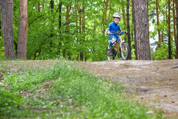 Obraz premium Happy funny little kid boy in colorful raincoat riding his first bike on cold day in forest. Active leisure for children outdoors. Happy carefree childhood concept.