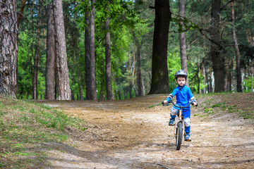 Happy cute blond kid boy having fun his first bike on sunny summer day, outdoors. Happy child making sports. Active leisure for children.Kid boy wear safety helmet. boy is smiling and cicling.