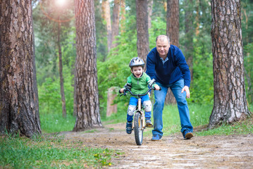 Little kid boy of 3 years and his father in autumn forest with a bicycle. Dad teaching his son. Man happy about success. Child with helmet. Safety, sports, leisure with kids concept.