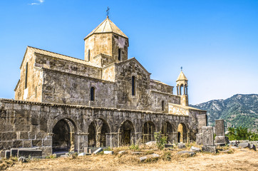 Fototapeta na wymiar Odzun monastery on the south side with views of the arched gallery with the bell tower and stone crosses in the background of forested mountains