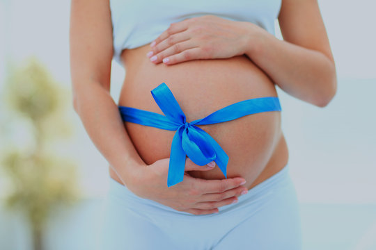 Woman Holding Hands On Her Baby Bump, Tied With A Blue Bow.