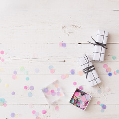 Top view on two Christmas or birthday gifts wrapped in black and white paper with box of party confetti on white wooden table