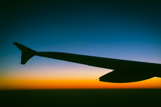 Silhouette of a jets wing against a cloudless gradient sunset that goes from orange to blue to black
