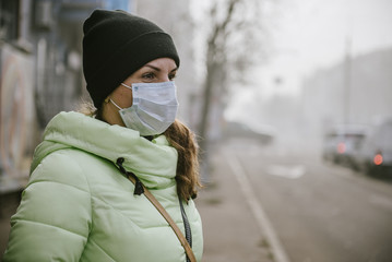 the girl is standing by the road in a protective medical mask.