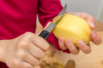 Nahaufnahme zweier Kinderhände, die eine Kartoffel mit einem scharfen Küchenmesser oder Schälmesser schälen