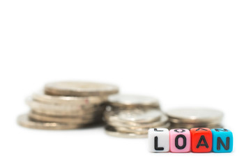 Close up image of the alphabet dices which are arranged for a word LOAN in front of stack of coins, and isolated on white background.