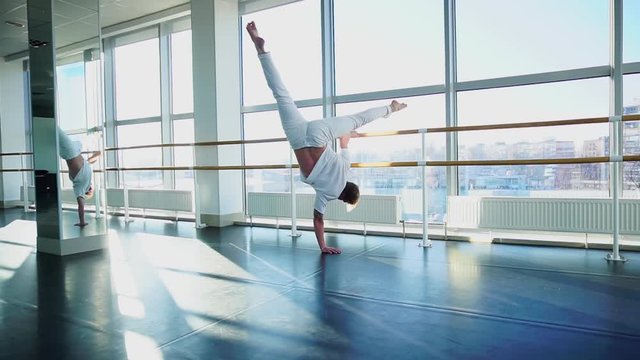 Male person doing one arm handstand with legs spread out.