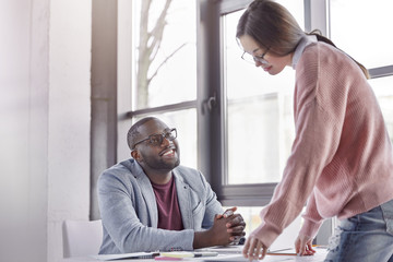 Cheerful African American male boss listens to his female secretary with happy expression, rejoices achievement great success and showing high results on business market, work at new startup