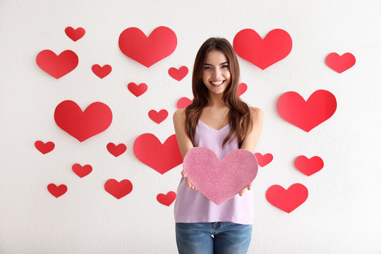 Romantic young woman with paper heart for Valentine's Day indoors
